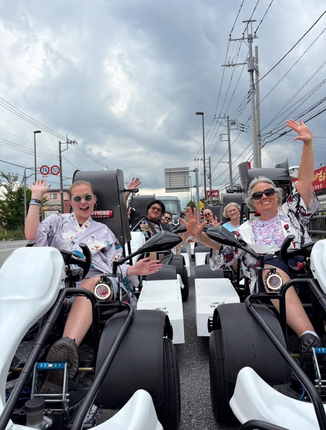 Smiling guests in kimono waving from electric go-karts on a Mt. Fuji tour